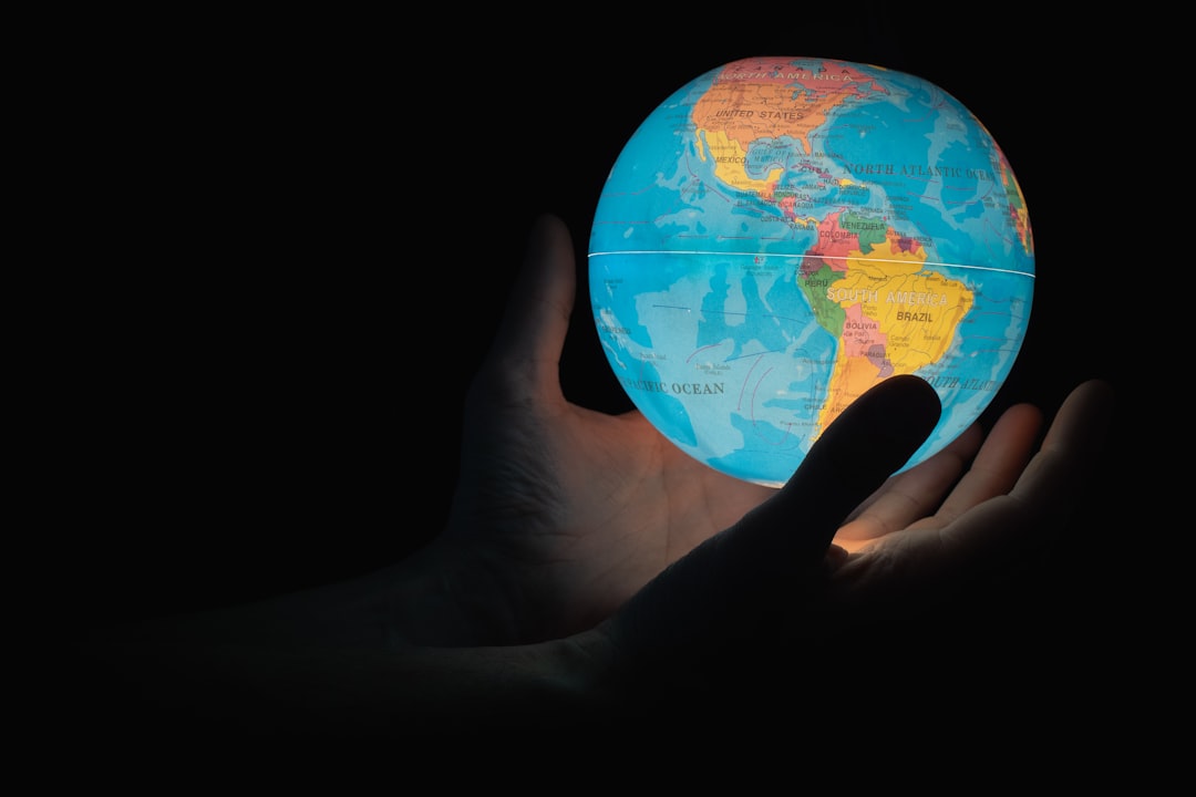 A hand holding a glowing globe depicting the Americas against a dark background.